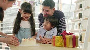 Happy Asian Thai family, young kids surprised by birthday cake, gift, blow out a candle, and celebrate party with parents and siblings together at dining table, wellbeing domestic home special event.