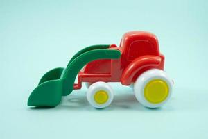 red paint plastic toy bulldozer with green universal blade isolated on turquoise photo