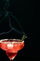 Alcoholic or non-alcoholic margarita type cocktail with ice and steaming rosemary branch on dark background