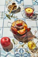 té de frutas con manzanas y tomillo en una tetera de vidrio y una taza sobre una mesa hecha de azulejos de colores foto