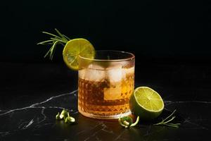 Alcoholic or non-alcoholic cocktail with lime and rosemary on a dark marble table photo