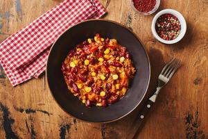 chili con carne con carne molida, frijoles y maíz en un tazón oscuro sobre fondo de madera. cocina mexicana y tejana foto