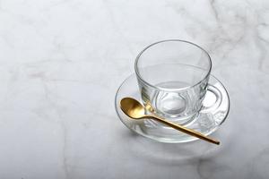 taza de vidrio vacía en platillo con cuchara dorada en mesa de mármol claro foto