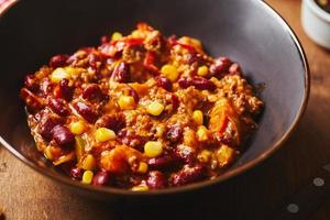 chili con carne con carne molida, frijoles y maíz en un tazón oscuro sobre fondo de madera. cocina mexicana y tejana foto