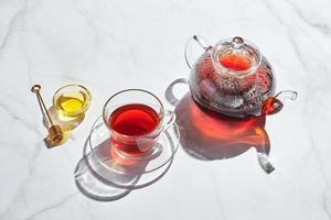 té de frutas con manzanas y tomillo y miel en tetera de vidrio y taza sobre fondo blanco con sombras duras