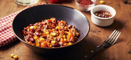 Chili Con Carne with ground beef, beans and corn in dark bowl on wooden background. Mexican and Texas cuisine