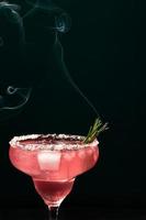 Alcoholic or non-alcoholic margarita type cocktail with ice and steaming rosemary branch on dark background photo