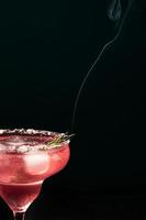 Alcoholic or non-alcoholic margarita type cocktail with ice and steaming rosemary branch on dark background photo