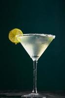 Glass of martini with cocktail or mocktail and lime wedge on dark background photo