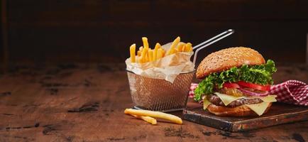 Homemade burger with beef, cheese and onion marmalade on a wooden board, fries in a metal basket. Fast food concept, american food