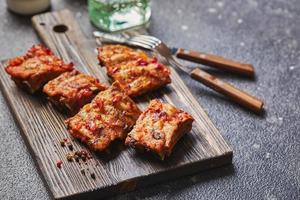 Grilled baked pork ribs with spices on wooden cutting board on dark background. American food concept. photo