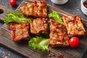 Grilled baked pork ribs with spices and vegetables on wooden cutting board on dark background. American food concept. photo
