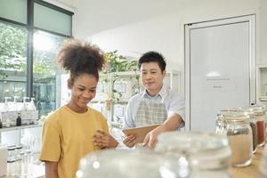 Asian male shopkeeper describes natural organic products to woman customer in refill store, zero-waste and plastic-free grocery, eco environment-friendly, sustainable lifestyles with a reusable shop. photo