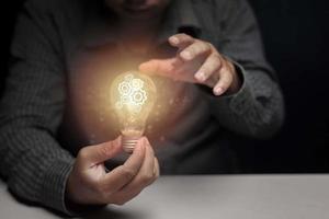 Man holding and showing a glowing light bulb Inside the dark room, the power of wisdom concept. photo
