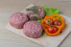 chuleta de hamburguesa cruda sobre tablero de madera y fondo de madera foto