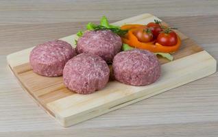 chuleta de hamburguesa cruda sobre tablero de madera y fondo de madera foto