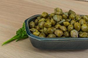 Capers in a bowl on wooden background photo