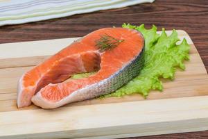 Raw salmon steak on wooden board and wooden background photo