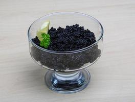 caviar negro en un recipiente sobre fondo de madera foto