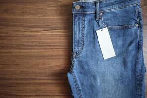 Blue jeans with blank white price label tag on wooden background photo