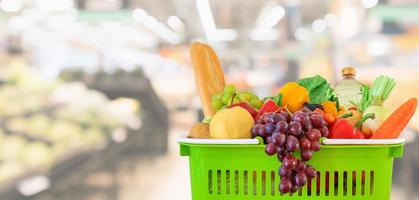 cesta de la compra llena de frutas y verduras con supermercado tienda de comestibles fondo desenfocado borroso con luz bokeh foto