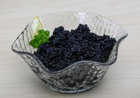 Black caviar in a bowl on wooden background photo