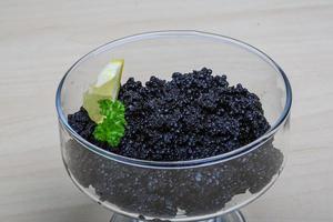 caviar negro en un recipiente sobre fondo de madera foto