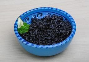 Black caviar in a bowl on wooden background photo