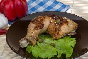 muslo de pollo asado en el plato y fondo de madera foto