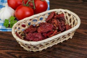 Dried tomtoes in a basket on wooden background photo