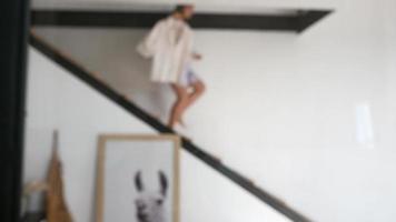 Young woman in sundress runs down stairs carrying clothes on a hanger video