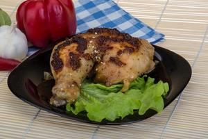 muslo de pollo asado en el plato y fondo de madera foto