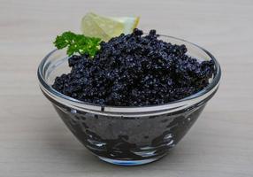 caviar negro en un recipiente sobre fondo de madera foto