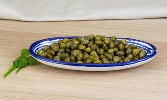 Capers in a bowl on wooden background photo