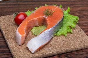 Raw salmon steak on wooden board and wooden background photo