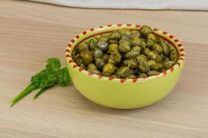 Capers in a bowl on wooden background photo