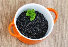 caviar negro en un recipiente sobre fondo de madera foto