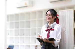 Young asian business woman is standing at a desk and taking notes in a notebook. The concept of education and technology. photo