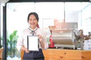 portrait of a woman wearing an apron holding a digital tablet with a blank white screen. Waiter holding a touch screen tab with copy space for your text. photo