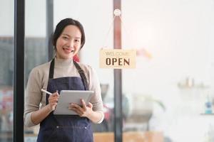 Startup successful small business owner sme beauty girl stand with tablet smartphone in coffee shop restaurant. Portrait of asian tan woman barista cafe owner. SME entrepreneur seller business concept photo