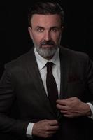 Portrait of a stylish elegant senior businessman with a beard and casual business clothes in photo studio adjusting suit