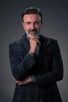 Portrait of a stylish elegant senior businessman with a beard and casual business clothes in photo studio isolated on dark background gesturing with hands