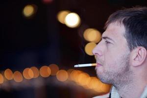 el hombre fuma un cigarrillo contra un fondo oscuro foto