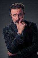 Portrait of a stylish elegant senior businessman with a beard and casual business clothes in photo studio isolated on dark background gesturing with hands