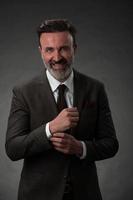 Portrait of a stylish elegant senior businessman with a beard and casual business clothes in photo studio adjusting suit