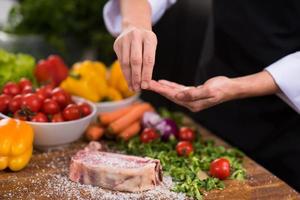 Chef putting salt on juicy slice of raw steak photo