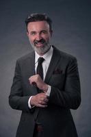 Portrait of a stylish elegant senior businessman with a beard and casual business clothes in photo studio isolated on dark background gesturing with hands