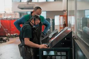 two workers wearing a face mask due to a coronavirus pandemic are programming a modern cnc machine photo