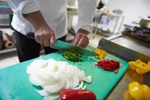 chef en la cocina del hotel cortar verduras con cuchillo foto