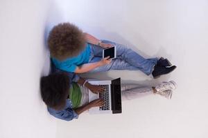 pareja multiétnica sentada en el suelo con una computadora portátil y una vista superior de la tableta foto